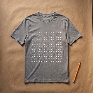 Mid heather grey t-shirt with the white generative triangle grid print, flat lay on kraft paper with a pencil
