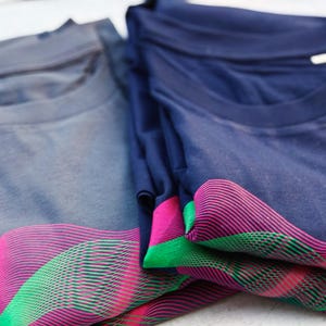 Close-up of folded grey and navy t-shirts with the pink and green psychedelic wave lines
