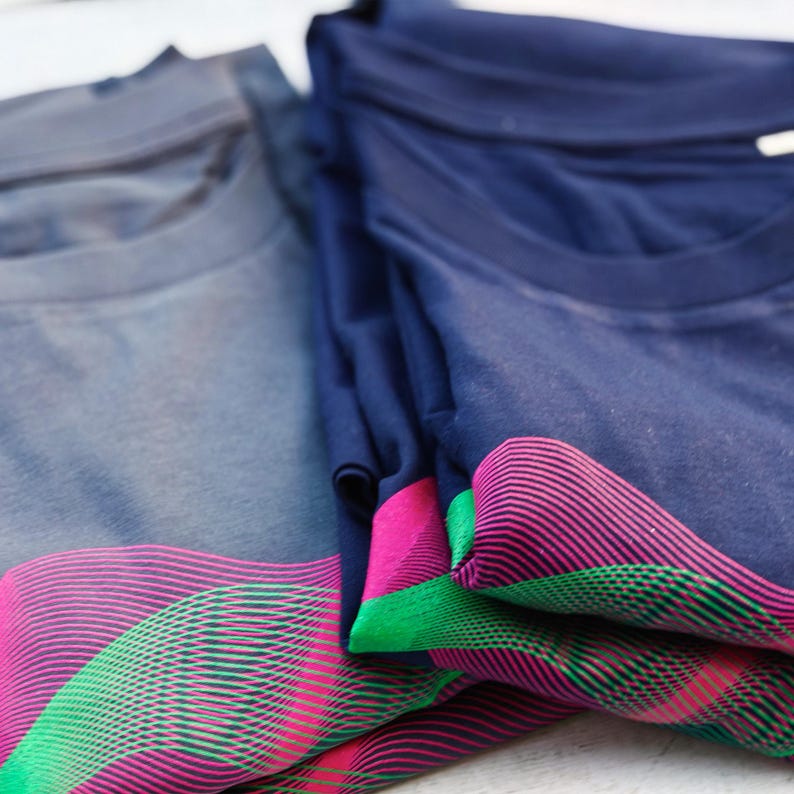 Close-up of folded grey and navy t-shirts with the pink and green psychedelic wave lines