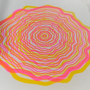 Close-up of the A5 riso print showing the grainy risograph ink texture, concentric tree rings in pink and yellow