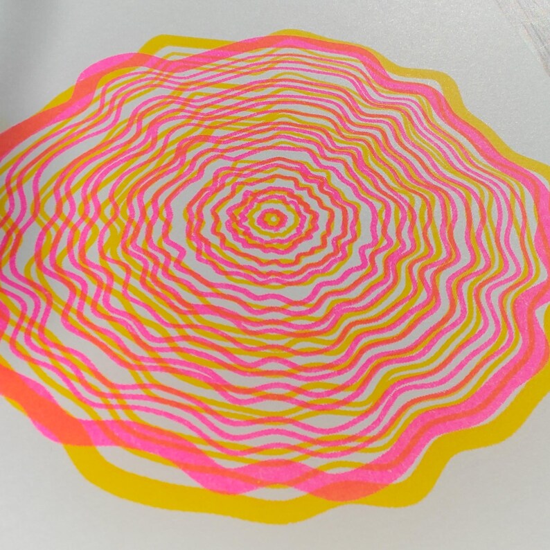 Close-up of the A5 riso print showing the grainy risograph ink texture, concentric tree rings in pink and yellow