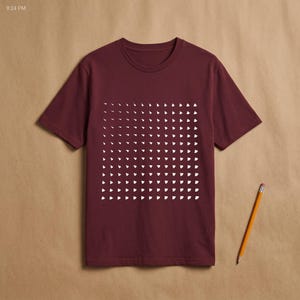 Burgundy t-shirt with the white generative triangle grid print, flat lay on kraft paper with a pencil beside it