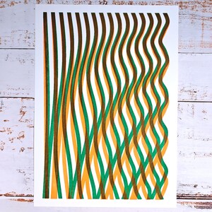 Handmade A3 risograph print with wavy green, yellow-orange and brown lines lying flat on a whitewashed wooden surface