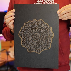 May include: A black poster with a gold metallic design of a circular pattern with concentric rings. The design resembles a tree ring.