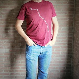 May include: A maroon t-shirt with a white graphic design of a winding line.