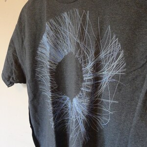 Close-up of the blue radial circle print on the dark grey t-shirt — fine lines radiating outward from a central void