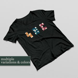 May include: Black t-shirt featuring the word "HIE" in a geometric design. The letters are made up of orange, blue, and pink shapes. The image also includes the text "multiple variations & colours".