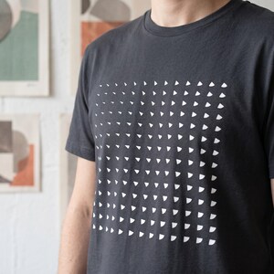 Man wearing the india ink grey t-shirt with the white rotating triangle pattern, white wall with art prints behind