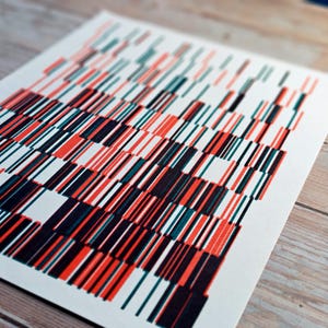 Könnte beinhalten: Abstrakter Kunstdruck mit einem Muster aus vertikalen Linien in Rot, Türkis, Schwarz und Weiß. Die Linien sind in einem rasterartigen Design angeordnet und erzeugen eine visuell dynamische Komposition. Das Kunstwerk ist auf weißem Papier gedruckt und auf einer Holzoberfläche ausgestellt.