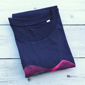 Folded navy t-shirt on white wood showing the pink and green wave print at the hem