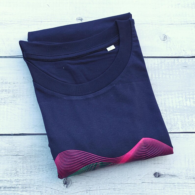 Folded navy t-shirt on white wood showing the pink and green wave print at the hem