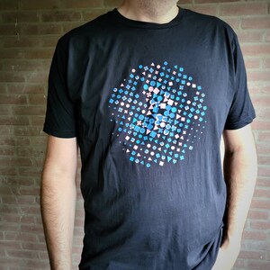 Peut inclure: Un t-shirt noir avec un motif circulaire composé de formes géométriques bleues, roses et blanches.