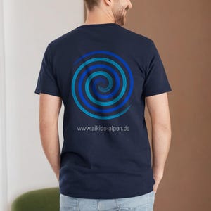 Peut inclure: Un t-shirt bleu marine avec un motif en spirale bleu et turquoise au dos. Le texte "www.aikido-alpen.de" est imprimé sous le motif.