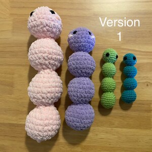 May include: Four crocheted stuffed toys in the shape of caterpillars. The largest caterpillar is pink, the next largest is purple, and the two smallest are green and blue.