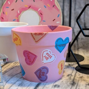 Puede incluir: Una taza de cerámica blanca con asa negra y el texto "But First, Coffee" en negrita negra. La taza está sobre un fondo borroso. La taza parece tener una capacidad de unos 355 ml.