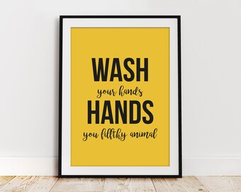 May include: A yellow poster with black text that reads "WASH your hands HANDS you filthy animal". The poster is framed in a black frame.
