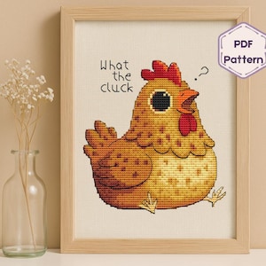 Può includere: Schema a punto croce di un pollo dei cartoni animati con la scritta "What the cluck" sopra. Il pollo è giallo e marrone con cresta e bargigli rossi. L'immagine è incorniciata in una cornice di legno chiaro.