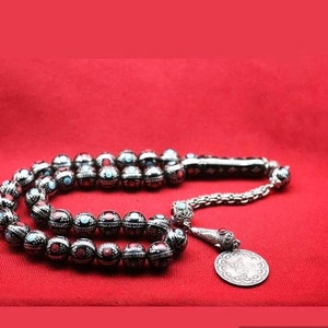 Può includere: Un rosario d'argento con perline nere e rosse, una catena d'argento e un ciondolo d'argento con disegni intricati.