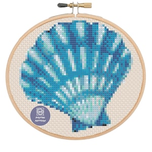 May include: A blue and green seashell cross stitch pattern in a wooden embroidery hoop. The pattern is a digital download.