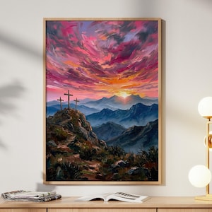 Könnte beinhalten: Ein gerahmtes Landschaftsgemälde zeigt drei Kreuze auf einem Berg, vor einem Sonnenuntergang in Rosa, Orange und Lila. Das Kunstwerk hängt über einem Holzschrank, zusammen mit einer goldenen Lampe und dekorativen Gegenständen.