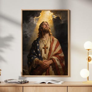 Könnte beinhalten: Gerahmtes Kunstwerk, das eine religiöse Figur mit langem Haar und Bart zeigt, die nach oben in Richtung eines hellen Lichts blickt. Die Figur ist in ein Gewand gehüllt, das die amerikanische Flagge zeigt. Das Kunstwerk wird auf einem hellen Holzschrank ausgestellt.