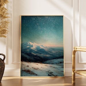 Könnte beinhalten: Ein gerahmter Kunstdruck zeigt eine schneebedeckte Bergkette unter einem sternenklaren Nachthimmel. Das Kunstwerk verwendet Blau-, Weiß- und Rosatöne mit einem goldenen Rahmen. Links befindet sich eine dekorative Vase mit getrockneten Pflanzen.