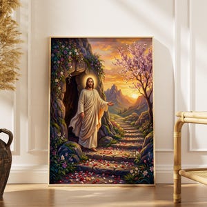 Könnte beinhalten: Ein gerahmtes Kunstwerk zeigt eine Figur in weißen Gewändern, die aus einer Höhle tritt und von goldenem Licht durchflutet wird. Die Szene umfasst einen Steinweg, blühende Blumen und einen lebendigen Sonnenuntergang über einer Bergkette. Das Kunstwerk wird auf einem Holzboden ausgestellt.