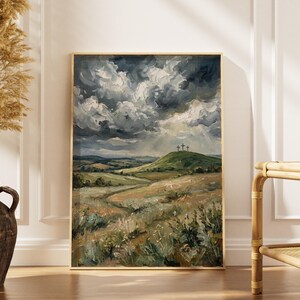 Könnte beinhalten: Gerahmtes Landschaftsgemälde mit einem grünen Hügel mit drei Kreuzen unter einem dramatischen, bewölkten Himmel. Das Kunstwerk befindet sich in einem goldenen Rahmen und lehnt an einer weißen Wand. Das Gemälde erzeugt Tiefe.