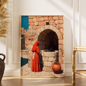 Könnte beinhalten: Ein gerahmter Druck zeigt eine Person in roter Robe in der Nähe eines Steinbrunnens. Das Kunstwerk zeigt einen Steinbogen und einen Terrakottatopf. Der Hintergrund zeigt einen blauen Himmel und Steingebäude, die eine historische Architekturszene schaffen.
