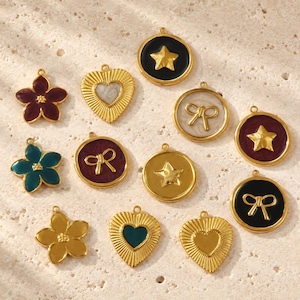 Peut inclure: Un ensemble de douze breloques en métal doré de formes variées, incluant des fleurs, des cœurs, des cercles et des étoiles. Ces breloques présentent des incrustations d'émail coloré en noir, rouge foncé, bleu sarcelle et crème, avec des motifs en relief.