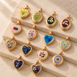 Puede incluir: Una colección de catorce relicarios de metal dorado con formas de corazón y ovaladas. Cada relicario presenta un diseño único de flores prensadas bajo una superficie transparente, mostrando varios colores florales como azul, rosa, amarillo y blanco.