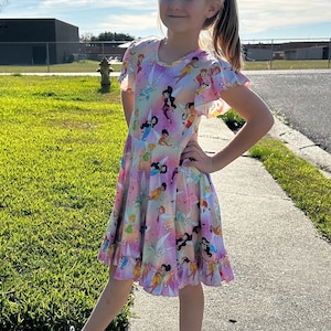 May include: A young girl wearing a pink and white dress with a print of fairies. The dress has short sleeves and a ruffled hem. She is wearing white trainers and has her hair pulled back in a ponytail.