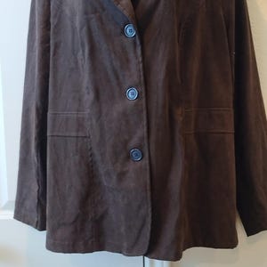 Peut inclure: Une veste en daim marron avec une fermeture à boutons et deux poches.