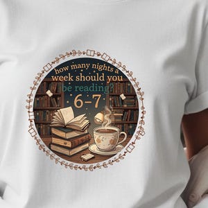 Puede incluir: Camiseta blanca con un diseño gráfico circular que presenta libros, una taza de té y el texto "how many nights a week should you be reading 6-7". La camiseta se combina con unos vaqueros azules.