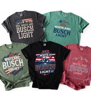 Puede incluir: Cinco camisetas de manga corta en gris carbón, verde, negro y rojo con estampados gráficos de montañas, elementos de la bandera estadounidense y el texto Red, White and Busch Light. Las camisetas tienen cuello redondo y corte holgado.