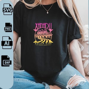 Puede incluir: Camiseta negra con un diseño gráfico colorido. El diseño muestra el texto "XANADU ROLLER RINK - LOS ANGELES, CALIFORNIA" y una ilustración de una pista de patinaje sobre ruedas en rosa, amarillo y naranja.
