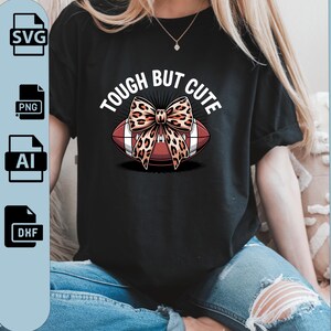 Puede incluir: Camiseta negra con el texto "TOUGH BUT CUTE" sobre un balón de fútbol con un lazo con estampado de leopardo. La imagen también incluye iconos de tipo de archivo de descarga digital: SVG, PNG, AI y DXF.