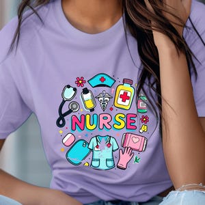 Puede incluir: Una camiseta morada con un diseño gráfico colorido que incluye un estetoscopio, píldoras, un corazón y la palabra "NURSE".