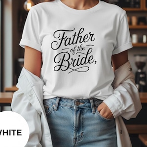 Puede incluir: Camiseta blanca con la frase "Father of the Bride" en escritura negra. La camiseta se combina con vaqueros azules y una chaqueta blanca. El estilo es casual y cómodo.
