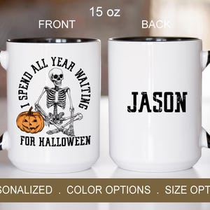 May include: A white ceramic coffee mug with a black rim and handle. The front of the mug features a skeleton holding a pumpkin with the text "I spend all year waiting for Halloween". The back of the mug has the name "Jason" in black text.