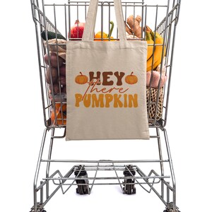 May include: A shopping cart filled with groceries, including produce, bananas, and a reusable tote bag with the text "Hey there Pumpkin" printed on it.