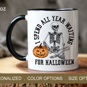 May include: White ceramic mug with a black handle. The mug has a skeleton sitting on a pumpkin with the text "I spend all year waiting for Halloween".