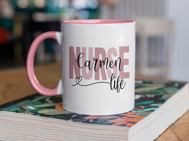 Puede incluir: Taza de cer&aacute;mica blanca con borde y asa de color rosa. La taza tiene el texto "Nurse Carmen life" impreso en rosa y negro.