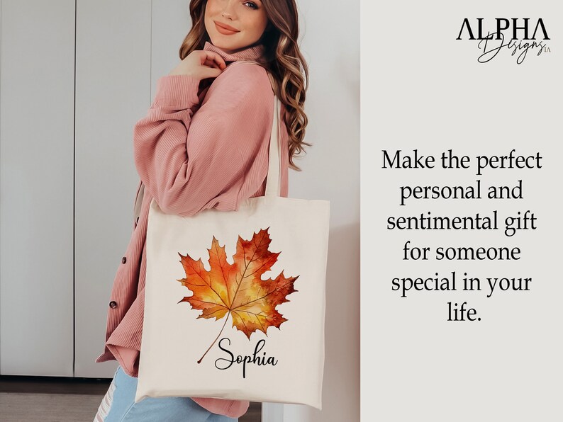 May include: A white tote bag featuring a watercolour illustration of an autumn leaf in shades of orange and yellow. The name "Sophia" is written in cursive below the leaf.