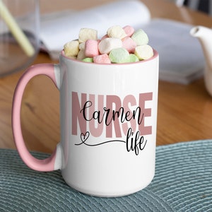 Puede incluir: Taza de cer&aacute;mica blanca con borde y asa de color rosa. La taza tiene el texto "NURSE carmen life" impreso en letras rosa y negras. La taza est&aacute; llena de malvaviscos.