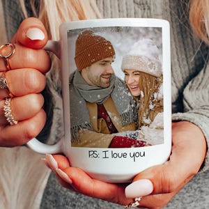 May include: White ceramic mug with a photo of a couple in winter clothing, smiling at each other. The text "P.S.: I love you" is printed on the mug.