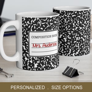 May include: White ceramic coffee mug with a black and white composition notebook design. The mug has a red inscription that reads "COMPOSITION BOOK" and "Mrs. Anderson".