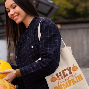 May include: A white canvas tote bag with the text "HEY there PUMPKIN" in orange and brown lettering. The bag features two small orange pumpkins with green stems.