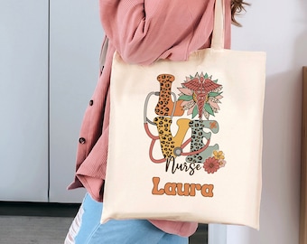 May include: A white canvas tote bag with a colorful graphic of the word "LOVE" with a stethoscope and a medical caduceus symbol. The text "Nurse Laura" is printed below the graphic.