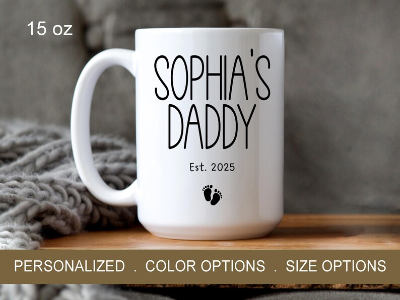 Peut inclure: Une tasse en c&eacute;ramique blanche avec du texte noir qui dit "Sophia's Daddy Est. 2025" et un petit graphique de pied. La tasse est de 15 onces.